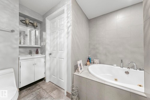Built-in soaking tub, large format tile walls, white vanity with integrated sink, chrome fixtures, and stone-finish flooring - 11119 31St Nw Nw, Edmonton, AB - Indoor Photo Showing Bathroom