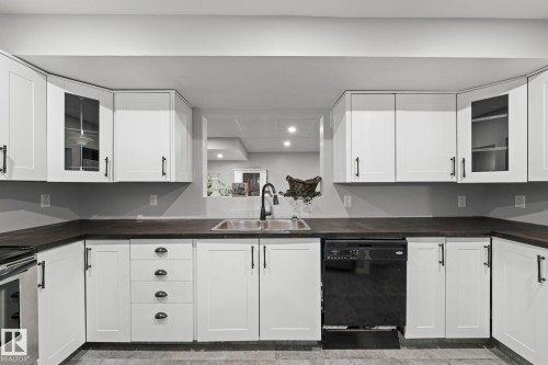 White shaker-style cabinetry with black hardware, dark countertops, an undermount sink with a black gooseneck faucet, and a built-in black dishwasher - 11119 31St Nw Nw, Edmonton, AB - Indoor Photo Showing Kitchen
