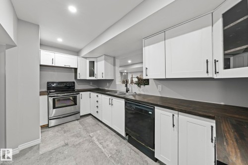 U-shaped kitchen featuring white cabinetry, dark wood-finish countertops, stainless steel range, and a black dishwasher - 11119 31St Nw Nw, Edmonton, AB - Indoor Photo Showing Kitchen With Double Sink