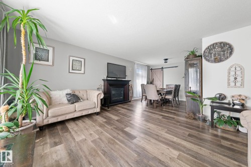Wood-finish flooring throughout, living area with fireplace, recessed light fixture, dining area with barn door, and large window with vertical blinds - 11119 31St Nw Nw, Edmonton, AB - Indoor Photo Showing Living Room With Fireplace