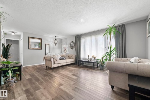 Spacious living area featuring wood-finish flooring, light gray wall paint, a large window with sheer and blackout curtains, and a prominent ceiling light fixture - 11119 31St Nw Nw, Edmonton, AB - Indoor Photo Showing Living Room