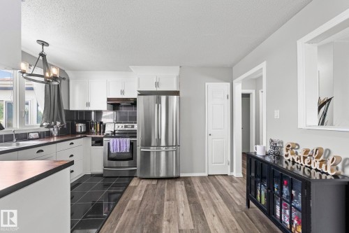 Modern kitchen featuring stainless steel appliances, white cabinetry, dark tile backsplash, wood-finish flooring, and a large window - 11119 31St Nw Nw, Edmonton, AB - Indoor Photo Showing Kitchen