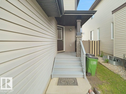 Front entrance featuring vinyl siding, covered porch, stone column accents, and a grey staircase with railing - 3010 17A Ave Nw, Edmonton, AB - Outdoor With Exterior