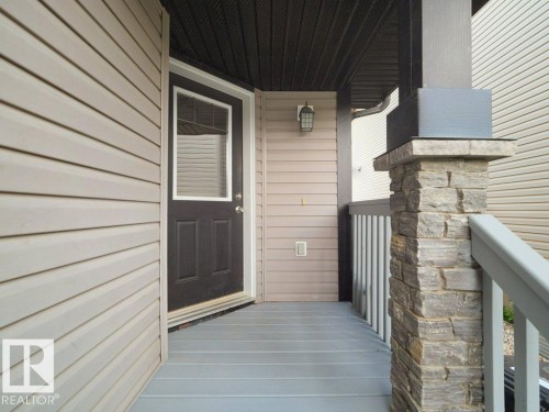 Covered entry featuring plank flooring, a detailed stone column, a dark wood-finish door with upper window, and horizontal siding - 3010 17A Ave Nw, Edmonton, AB - Outdoor With Exterior