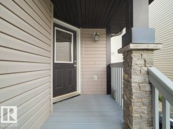 Covered entry featuring plank flooring, a detailed stone column, a dark wood-finish door with upper window, and horizontal siding - 