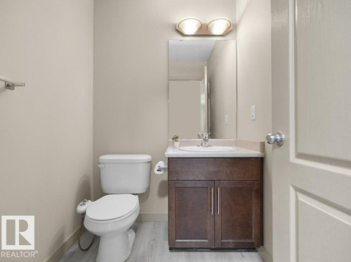 Wood-finish flooring with a white toilet, dark wood-finish vanity, integrated sink, and wall-mounted mirror - 3010 17A Ave Nw, Edmonton, AB - Indoor Photo Showing Bathroom