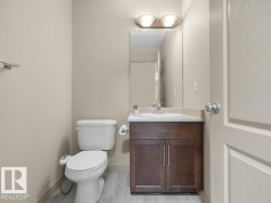 Wood-finish flooring with a white toilet, dark wood-finish vanity, integrated sink, and wall-mounted mirror - 