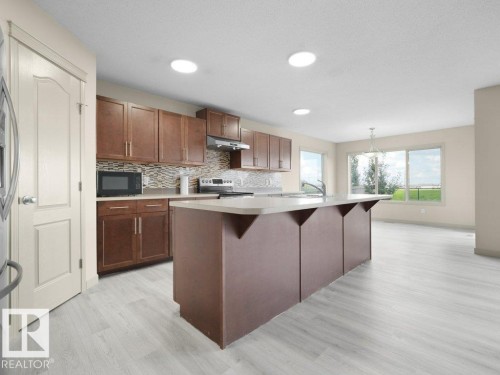 Open-concept kitchen with wood-finish flooring, recessed lighting, expansive windows, and a central island with integrated seating - 3010 17A Ave Nw, Edmonton, AB - Indoor Photo Showing Kitchen With Upgraded Kitchen