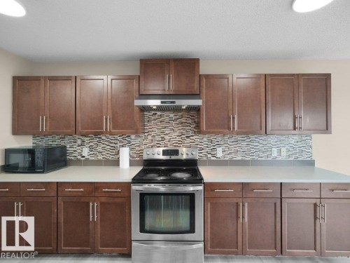 Stainless steel range with coordinating hood, extensive brown wood-finish cabinetry, light-toned countertops, and a patterned tile backsplash - 3010 17A Ave Nw, Edmonton, AB - Indoor Photo Showing Kitchen