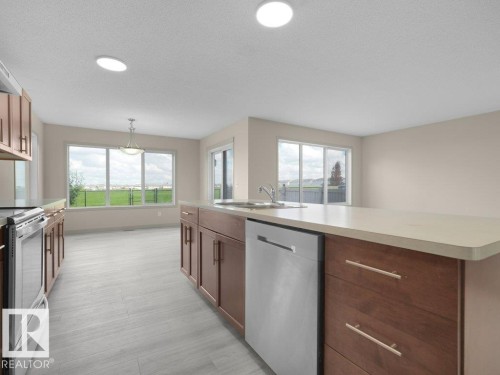 Open-concept kitchen featuring wood-finish cabinetry, stainless steel appliances, light-toned countertops, recessed lighting, and tile flooring - 3010 17A Ave Nw, Edmonton, AB - Indoor Photo Showing Kitchen