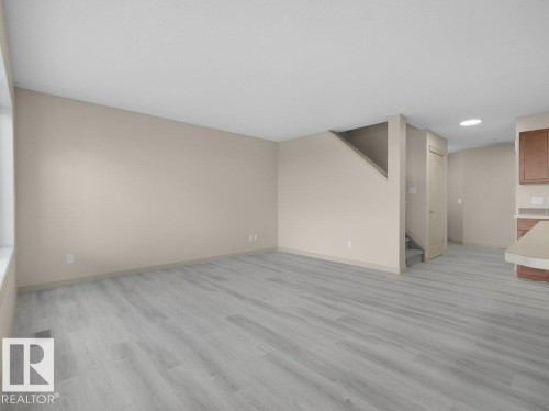 Expansive living area with light wood-finish flooring, neutral wall paint, and a large window - 3010 17A Ave Nw, Edmonton, AB - Indoor