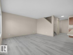 Expansive living area with light wood-finish flooring, neutral wall paint, and a large window - 