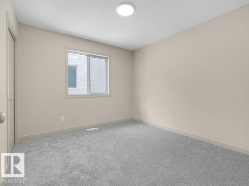 Neutral-toned walls, textured ceiling, light grey carpeting, and a window with a white frame - 3010 17A Ave Nw, Edmonton, AB - Indoor Photo Showing Other Room