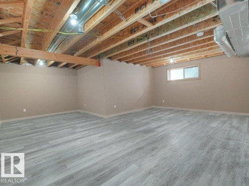 Spacious room featuring wood-finish flooring, neutral-toned walls, and exposed ceiling joists with visible ductwork - 3010 17A Ave Nw, Edmonton, AB - Indoor Photo Showing Basement
