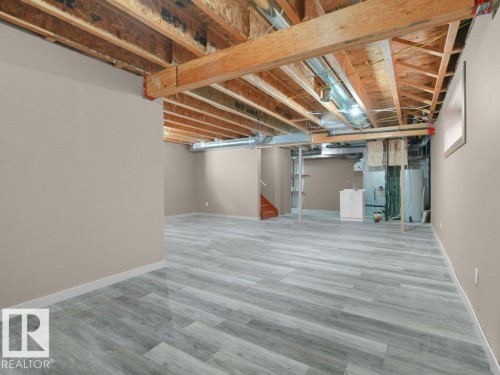 Spacious lower level with light gray wood-finish flooring, painted walls, exposed ceiling joists, and a utility area with a white cabinet - 3010 17A Ave Nw, Edmonton, AB - Indoor Photo Showing Basement