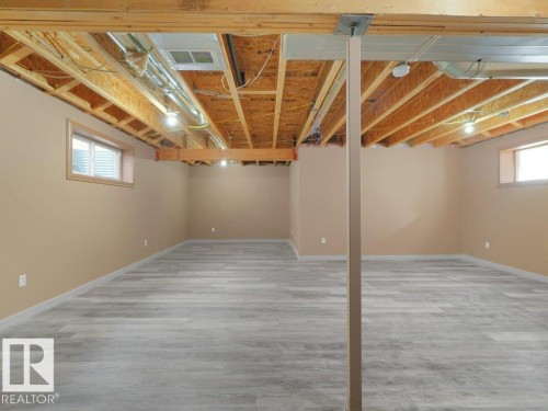 Finished lower level with wood-finish flooring, two windows, and exposed ceiling joists - 3010 17A Ave Nw, Edmonton, AB - Indoor Photo Showing Basement