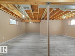 Finished lower level with wood-finish flooring, two windows, and exposed ceiling joists - 