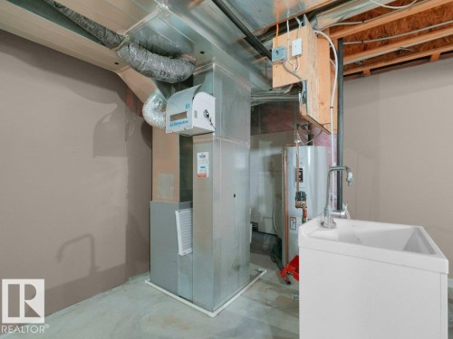 Galvanized sheet metal ductwork, furnace unit, water heater, and utility sink with a chrome faucet - 3010 17A Ave Nw, Edmonton, AB - Indoor Photo Showing Laundry Room