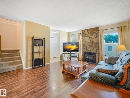 Stone-faced fireplace with a gas insert, wood-finish flooring, and carpeted stairs - 18417 66 Avenue Nw, Edmonton, AB - Indoor Photo Showing Living Room With Fireplace