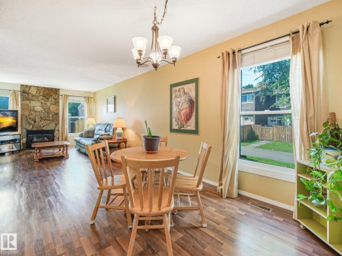 Open-concept living area featuring wood-finish flooring, a stone-accented fireplace, and multiple windows with exterior views - 18417 66 Avenue Nw, Edmonton, AB - Indoor Photo Showing Dining Room With Fireplace