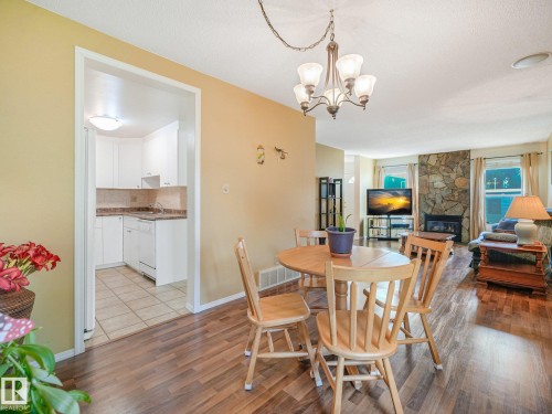Wood-finish flooring throughout, a stone-clad fireplace, and a kitchen featuring white cabinetry, a light-colored countertop, and tiled flooring - 18417 66 Avenue Nw, Edmonton, AB - Indoor Photo Showing Dining Room With Fireplace