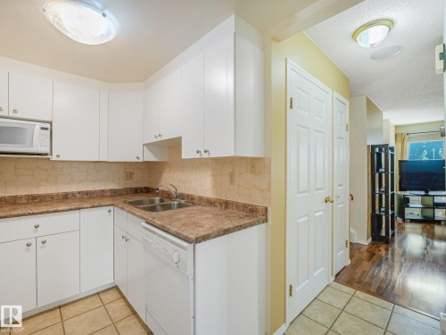 White cabinetry with brushed nickel hardware, a double basin stainless steel sink, tile backsplash, and a built-in dishwasher - 18417 66 Avenue Nw, Edmonton, AB - Indoor Photo Showing Kitchen With Double Sink