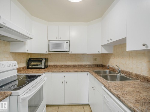 Efficient kitchen featuring white cabinetry, stone-look countertops, tiled backsplash, a built-in microwave, and a dual basin sink - 18417 66 Avenue Nw, Edmonton, AB - Indoor Photo Showing Kitchen With Double Sink