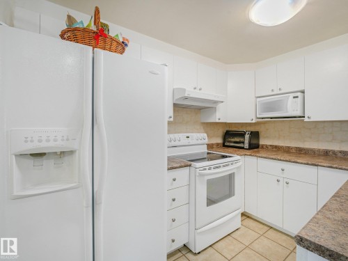 White cabinetry, built-in microwave, white electric range, tiled flooring, and light-toned countertops - 18417 66 Avenue Nw, Edmonton, AB - Indoor Photo Showing Kitchen