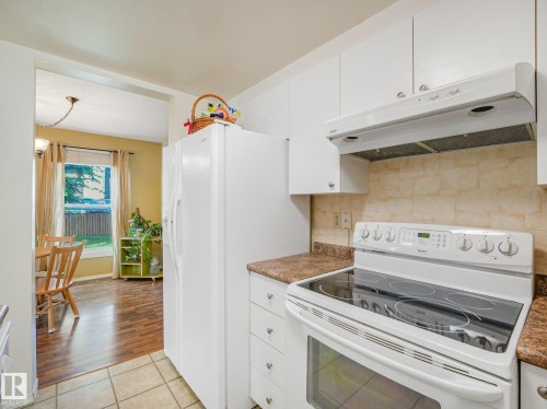 Kitchen featuring white cabinetry, brown-toned countertops, tile backsplash, and a white electric range with a coordinating range hood - 18417 66 Avenue Nw, Edmonton, AB - Indoor Photo Showing Kitchen