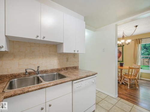 White cabinetry with chrome hardware, dual basin stainless steel sink, patterned countertop, and a tiled backsplash - 18417 66 Avenue Nw, Edmonton, AB - Indoor Photo Showing Kitchen With Double Sink