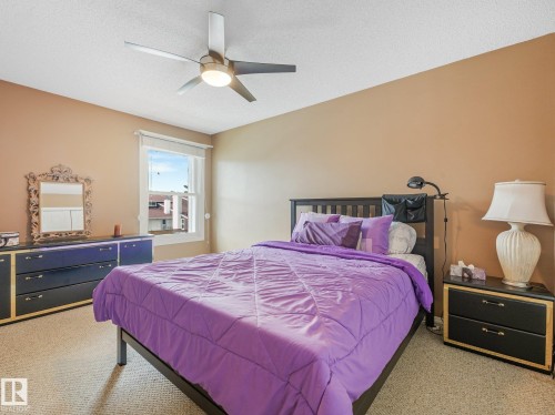 Ceiling fan with integrated lighting, window with white trim, tan wall paint, carpet flooring, and a built-in dresser - 18417 66 Avenue Nw, Edmonton, AB - Indoor Photo Showing Bedroom