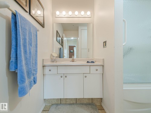 White vanity with a built-in sink and countertop, featuring a large mirror and overhead light fixture - 18417 66 Avenue Nw, Edmonton, AB - Indoor Photo Showing Bathroom