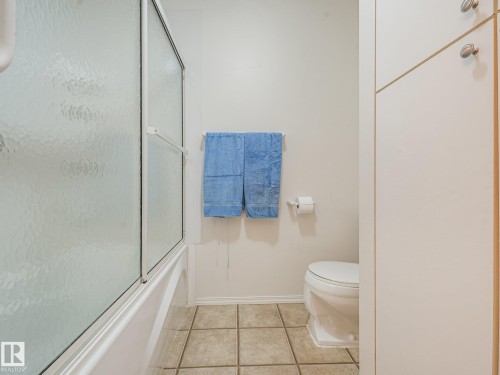 Bathtub with sliding shower door, tile flooring, toilet, and built-in vertical cabinetry - 18417 66 Avenue Nw, Edmonton, AB - Indoor Photo Showing Bathroom