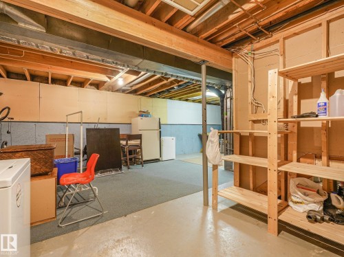 Unfinished basement with exposed ceiling joists, concrete flooring, and built-in wood shelving - 18417 66 Avenue Nw, Edmonton, AB - Indoor Photo Showing Basement