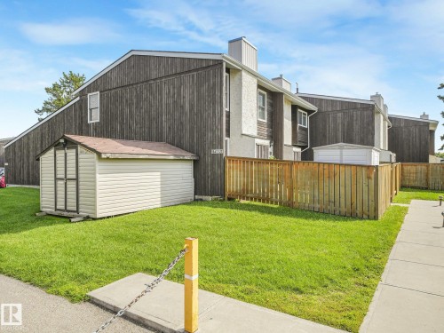 Exterior featuring vertical wood-finish siding, a private fenced yard, a storage shed, and a concrete pathway - 18417 66 Avenue Nw, Edmonton, AB - Outdoor With Exterior