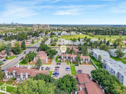Aerial perspective of a multi-unit property within a residential neighborhood, featuring established trees, paved parking areas, and nearby green spaces - 18417 66 Avenue Nw, Edmonton, AB - Outdoor With View