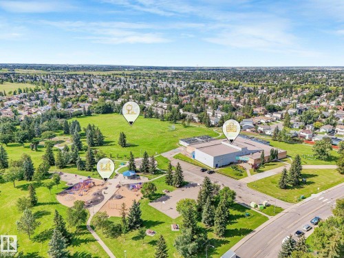 Expansive green spaces with mature trees, a dedicated playground area, a large institutional building, and surrounding residential structures - 18417 66 Avenue Nw, Edmonton, AB - Outdoor With View
