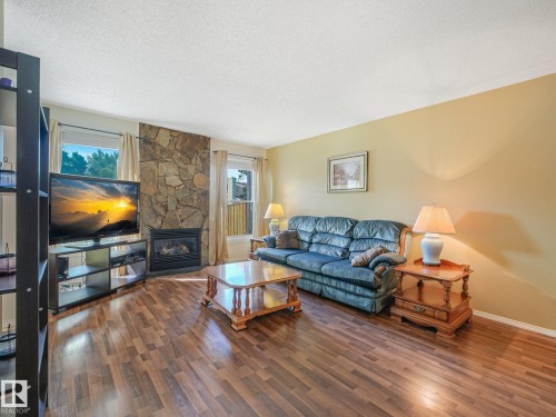 Wood-finish flooring, stone-clad fireplace with black insert, multiple windows, and light-toned wall paint - 18417 66 Avenue Nw, Edmonton, AB - Indoor Photo Showing Living Room With Fireplace