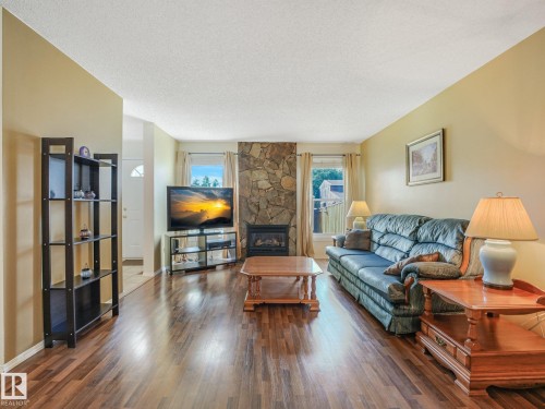 Wood-finish flooring, stone-clad fireplace, and multiple windows with exterior views - 18417 66 Avenue Nw, Edmonton, AB - Indoor Photo Showing Living Room With Fireplace