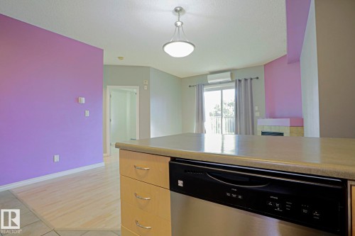 Kitchen island with integrated dishwasher, wood-finish flooring, built-in fireplace, and sliding glass door to exterior - #101 10118 95 St Nw Nw, Edmonton, AB - Indoor Photo Showing Kitchen
