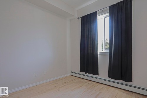 Hardwood-finish flooring with white baseboards, bright white walls, and a window with a sill - #101 10118 95 St Nw Nw, Edmonton, AB - Indoor Photo Showing Other Room