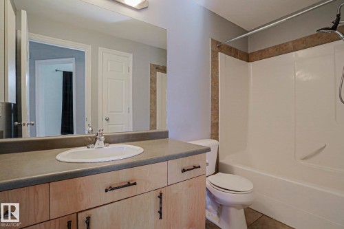 Bathroom featuring a light wood-finish vanity with a single basin sink, a neutral-toned countertop, and a shower-over-tub combination with tile surround - #101 10118 95 St Nw Nw, Edmonton, AB - Indoor Photo Showing Bathroom