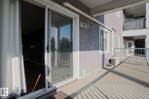 Exterior balcony with concrete flooring and metal railings, featuring a sliding glass door and an exterior wall light fixture - #101 10118 95 St Nw Nw, Edmonton, AB - Outdoor With Balcony With Exterior