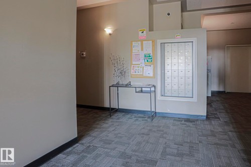 Wall-mounted mailboxes, bulletin board, wall sconce lighting, and patterned carpet flooring - #101 10118 95 St Nw Nw, Edmonton, AB - Indoor Photo Showing Other Room