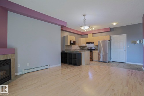 Open-concept living space featuring wood-finish flooring, a kitchen with stainless steel appliances, a breakfast bar, and a fireplace with a stone surround - #101 10118 95 St Nw Nw, Edmonton, AB - Indoor Photo Showing Kitchen With Fireplace