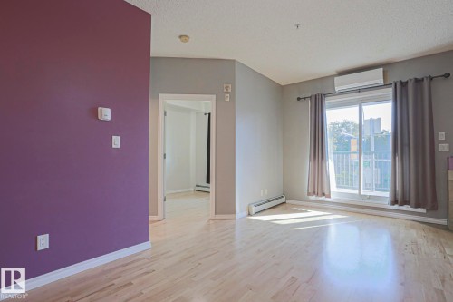 Hardwood-finish flooring, sliding glass door, wall-mounted air conditioning unit, and a painted accent wall - #101 10118 95 St Nw Nw, Edmonton, AB - Indoor Photo Showing Other Room