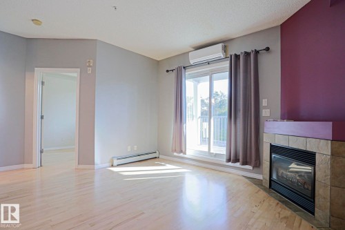 Hardwood flooring, tiled fireplace surround, glass sliding doors to a balcony, and a wall-mounted air conditioning unit - #101 10118 95 St Nw Nw, Edmonton, AB - Indoor With Fireplace