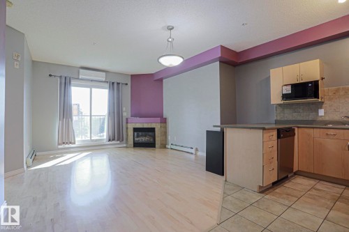 Open-concept living area featuring wood-finish flooring, a stone-surround fireplace, and a large sliding glass door - #101 10118 95 St Nw Nw, Edmonton, AB - Indoor Photo Showing Kitchen With Fireplace With Double Sink