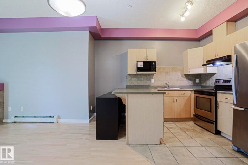 Kitchen featuring light-tone cabinetry, stainless steel appliances, stone-look countertops, and tile flooring - #101 10118 95 St Nw Nw, Edmonton, AB - Indoor Photo Showing Kitchen