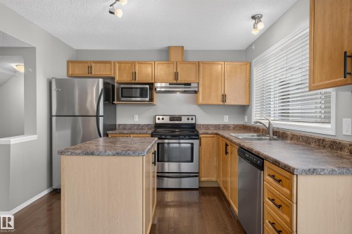 Kitchen featuring light wood-finish cabinetry, stainless steel appliances, dark wood-finish flooring, and a central island with a contrasting countertop - 6008 South Terwillegar Boulevard Nw, Edmonton, AB - Indoor Photo Showing Kitchen With Double Sink